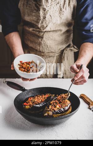 Preparazione delle melanzane farcite con carne macinata, pomodori e spezie. Piatto tradizionale Karniyarik di cucina turca Foto Stock