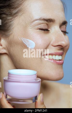 donna sorridente moderna di 40 anni con vasetto crema cosmetica su sfondo blu. Foto Stock