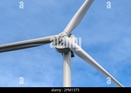 Primo piano di una turbina eolica di grandi dimensioni, guardando verso l'alto da un angolo. Cielo blu dietro con nuvola sottile. Foto Stock