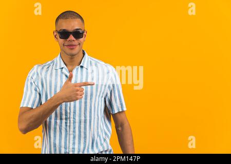Uomo afroamericano in occhiali da sole che punta sul lato su sfondo arancione. Foto di alta qualità Foto Stock