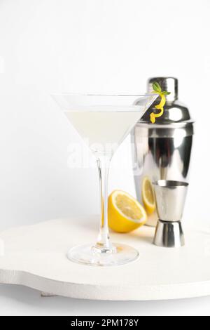 Bicchiere di gustoso martini, jigger, shaker e limone su sfondo bianco Foto Stock