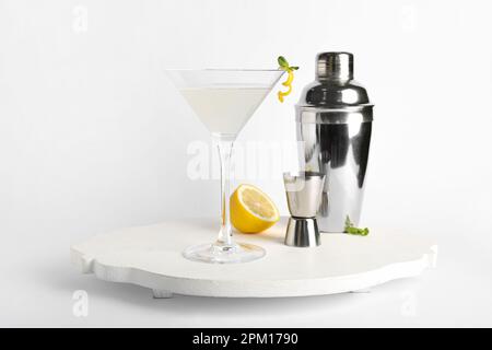 Bicchiere di gustoso martini, jigger, shaker e limone su sfondo bianco Foto Stock