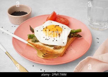 Delizioso sandwich con uova fritte, asparagi e pomodori su sfondo grigio Foto Stock