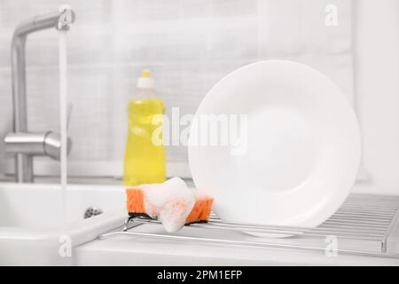 Cestello di asciugatura con piastra pulita e spugna saponata in un'elegante cucina Foto Stock