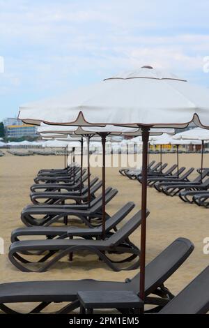 Molti bellissimi ombrelloni bianchi e lettini neri sulla spiaggia Foto Stock