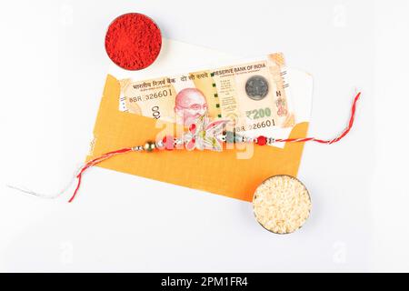 Vista dall'alto di rakhi con kumkum e denaro shagun su sfondo bianco, concetto di bandhan di raksha Foto Stock