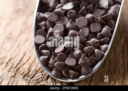 Gocce di cioccolato o bocconcini in metallo su legno (fuoco selettivo, focalizzazione di un terzo nelle gocce di cioccolato) Foto Stock