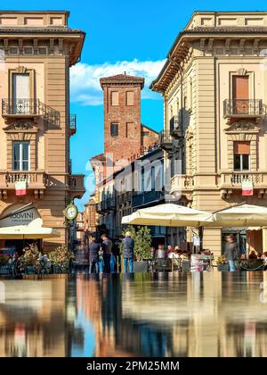 Edifici storici e torre medievale sullo sfondo sotto il cielo blu nel centro storico di Alba, Italia. Foto Stock