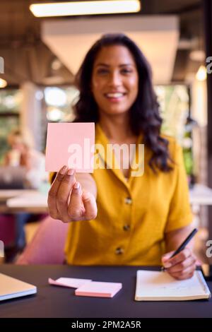 Ritratto di Businesswoman maturo che lavora alla scrivania in ufficio tenere in su vuoto Sticky Note Foto Stock