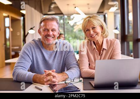 Ritratto di colleghi uomini e donne maturi di affari riunione intorno al laptop in ufficio moderno Foto Stock