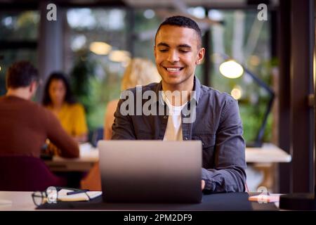 Giovane uomo d'affari che lavora sul laptop alla scrivania in ufficio Foto Stock