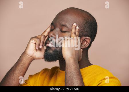 Uomo afroamericano che si concentra con gli occhi chiusi e pensando a qualcosa su sfondo marrone Foto Stock