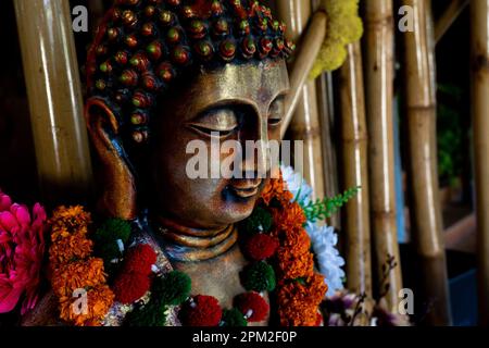 Primo piano della statua di buddha di bronzo seduta in meditazione con decorazioni floreali per la cerimonia del festival. Foto di alta qualità Foto Stock