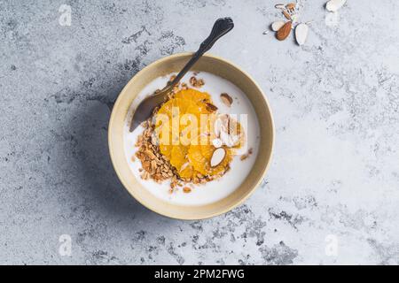 Ciotole di muesli allo yogurt con frutta arancione su tavola grigia, vista dall'alto. Sana colazione vegetariana pasto Foto Stock