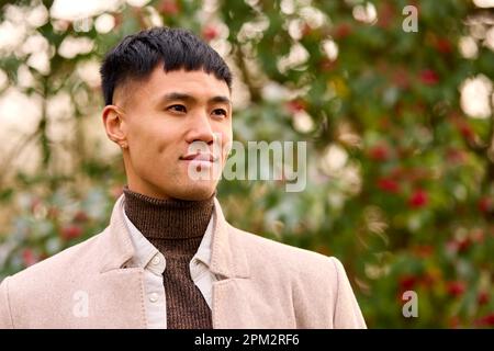 Giovane uomo sorridente che indossa un cappotto in piedi all'esterno nella campagna autunnale o invernale Foto Stock