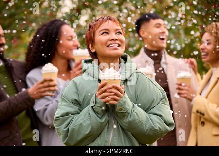 Gruppo di amici che indossano cappotti in piedi all'esterno in Snow Holding bevande calde al cioccolato Foto Stock