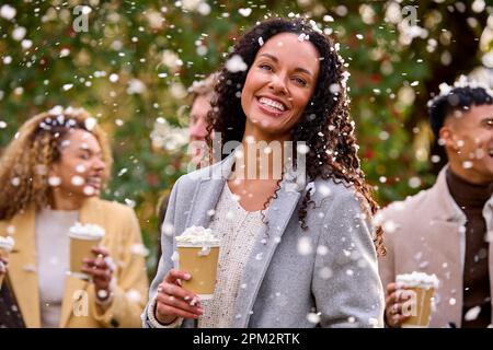 Gruppo di amici che indossano cappotti in piedi all'esterno in Snow Holding bevande calde al cioccolato Foto Stock