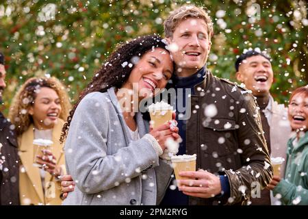 Gruppo di amici che indossano cappotti in piedi all'esterno in Snow Holding bevande calde al cioccolato Foto Stock