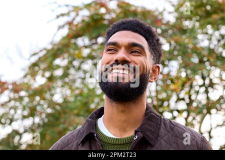 Giovane uomo sorridente che indossa un cappotto in piedi all'esterno nella campagna autunnale o invernale Foto Stock