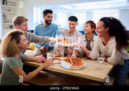 Amici divertirsi a casa in cucina mangiare pizze fatte in casa Foto Stock