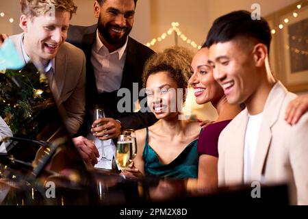 Gruppo di amici intorno al piano che festeggia insieme a Natale o Capodanno Foto Stock