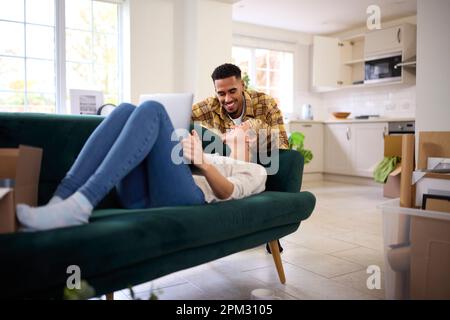 Accoppia disimballando le scatole dopo essere passato in Nuova Casa insieme come Donna si trova sul divano utilizzando il notebook Foto Stock