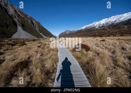 Il Boardwalk percorso con ombra di fotografo con fotocamera, Hooker Valley a piedi, dal Parco Nazionale Aoraki/Mount Cook, Alpi del sud, Canterbury, Isola del Sud, Foto Stock