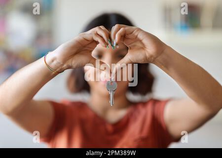 Donna araba allegra che tiene la chiave domestica e che mostra la gesture del cuore con le mani Foto Stock