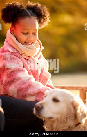 Ragazza seduta sul banco accarezzando cane da compagnia a piedi nella campagna autunnale Foto Stock