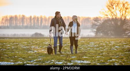 Coppia affettuosa con il cane Spaniel dell'animale domestico sulla camminata innevata nella campagna di inverno Foto Stock