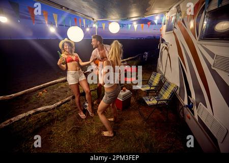 Gruppo di amici che hanno festa al tramonto sulla spiaggia; concetto di stile di vita informale Foto Stock