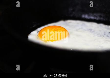 Uovo fritto in padella. Notte nera. Un uovo fritto in una padella di ghisa cosparso di pepe nero macinato. Fuori fuoco. Foto Stock