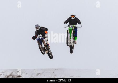 due motociclisti che saltano insieme su trampolino innevato, corse invernali di motociclette fuoristrada Foto Stock