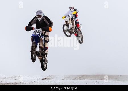 due motociclisti che saltano insieme su trampolino innevato, corse invernali di motociclette fuoristrada Foto Stock