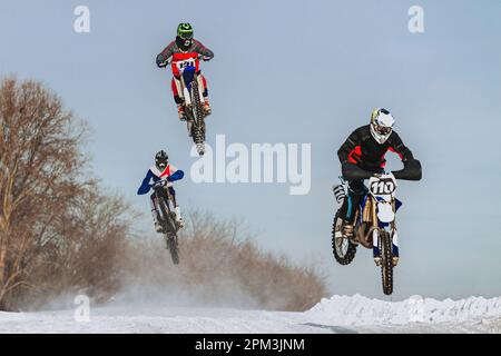 gruppo di motociclisti che saltano su trampolino innevato, corse di motocicli fuoristrada invernali Foto Stock