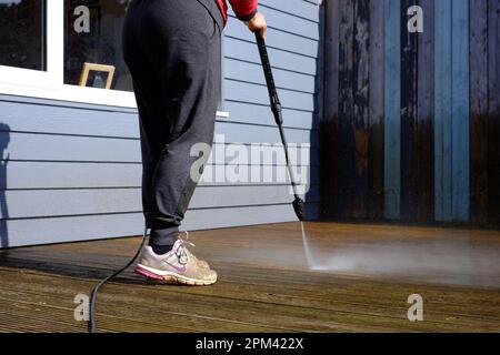 Donna che pulisce il ponte di legno con una idropulitrice Foto Stock