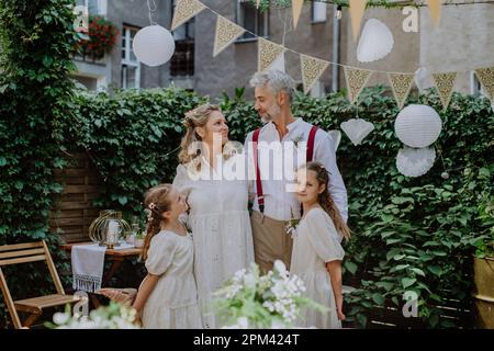 Sposa matura e sposo in posa con le loro figlie al ricevimento di nozze all'esterno nel cortile. Foto Stock