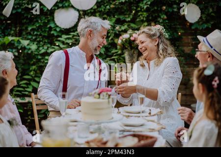 Sposa matura e sposi con gli ospiti al ricevimento di nozze all'esterno nel cortile. Foto Stock