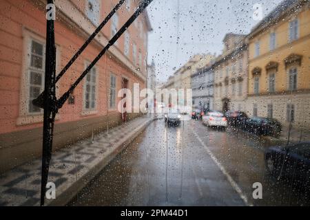 Pioggia in città. Focalizzazione selettiva sulle gocce di pioggia sulla finestra del tram contro il traffico su una strada urbana trafficata nelle giornate di pioggia. Foto Stock