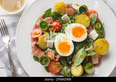 Insalata fatta in casa con verdure, pancetta, formaggio e uova sode condite con salsa di vinaigrette primo piano su un piatto sul tavolo. Orizzontale in alto vi Foto Stock