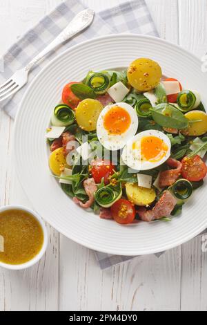 Insalata di contadini preparata con verdure a foglia, prosciutto, formaggio, pomodori, patate e uova bollite al primo piano sul tavolo. Vista verticale dall'alto Foto Stock