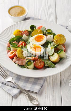 Insalata di contadini freschi con rucola, spinaci, patate, pancetta, pomodori, formaggio e uova sode primo piano su un piatto sul tavolo. Verticale Foto Stock