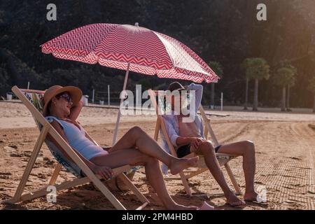 Coppia anziana seduta sulle sedie a sdraio e con un po' di relax al sole. Concetto: Pensione, giorno di spiaggia, tranquillità Foto Stock