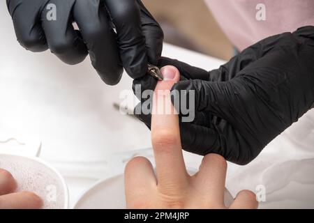 Manicurista che rimuove la cuticola dalle unghie femminili da un pestello di metallo durante l'immersione delle unghie nel bagno al salone delle unghie. Mani durante una cura manicure sessi Foto Stock