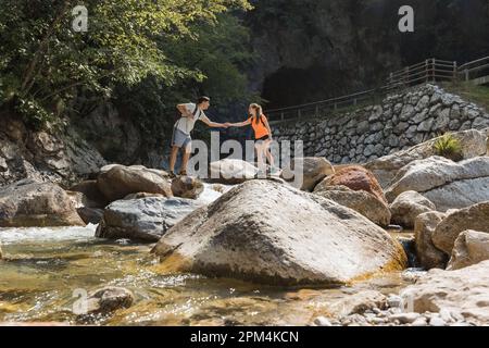 Coppia di escursionisti che cammina sulle rocce mentre attraversa il fiume di montagna, passando per un tour a piedi attraverso la gola. Concetto di stile di vita di viaggio e avventura. Foto Stock