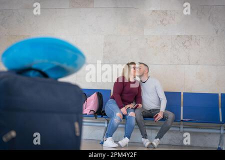 Un ragazzo dà alla sua ragazza un bacio sulla guancia mentre sono all'aeroporto in attesa di viaggiare Foto Stock