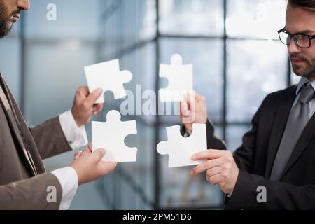 Lavorare insieme per mettere insieme le cose. due uomini d'affari irriconoscibili che uniscono pezzi di puzzle in studio Foto Stock