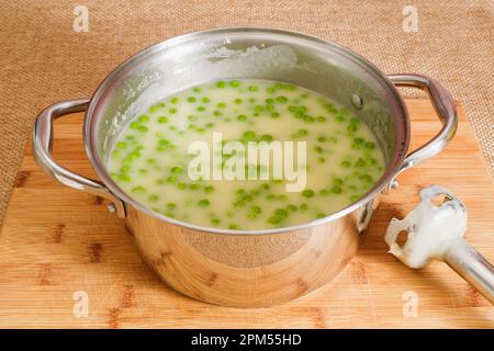 Zuppa di crema di sedano con piselli verdi in primo piano in una padella su sfondo rustico di legno Foto Stock