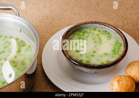 Zuppa di sedano con piselli verdi servita con pane al formaggio appena sfornato primo piano sul tavolo da cucina Foto Stock