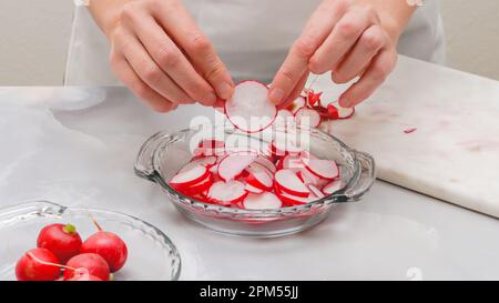 Ravanello fresco affettato primo piano su tagliere in marmo su sfondo grigio chiaro. Preparazione insalata vegetale, ricetta Foto Stock